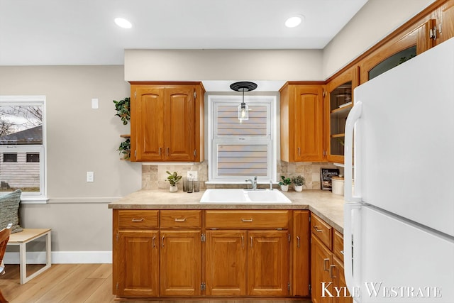 kitchen with tasteful backsplash, brown cabinetry, freestanding refrigerator, light wood-type flooring, and a sink