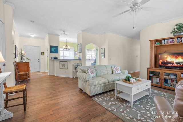 living room with arched walkways, ornamental molding, wood finished floors, baseboards, and ceiling fan with notable chandelier