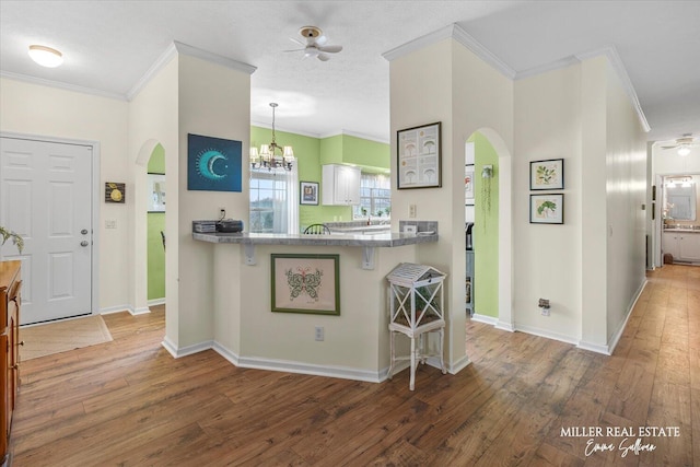 kitchen featuring a kitchen bar, arched walkways, crown molding, and ceiling fan with notable chandelier