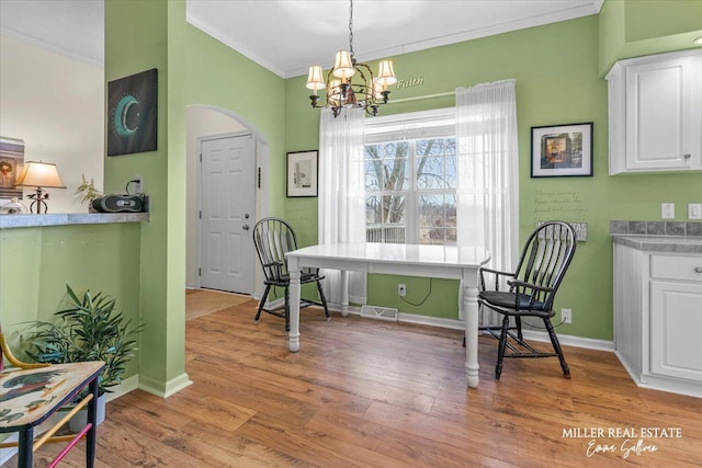 dining space with arched walkways, visible vents, an inviting chandelier, ornamental molding, and light wood-style floors