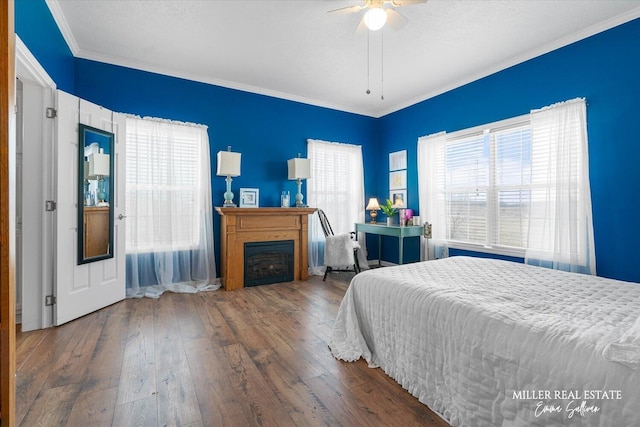 bedroom featuring ceiling fan, a textured ceiling, a fireplace, wood-type flooring, and crown molding