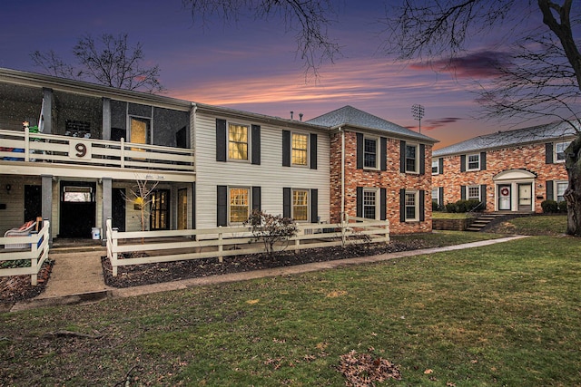 rear view of property with a balcony, fence, a lawn, and brick siding