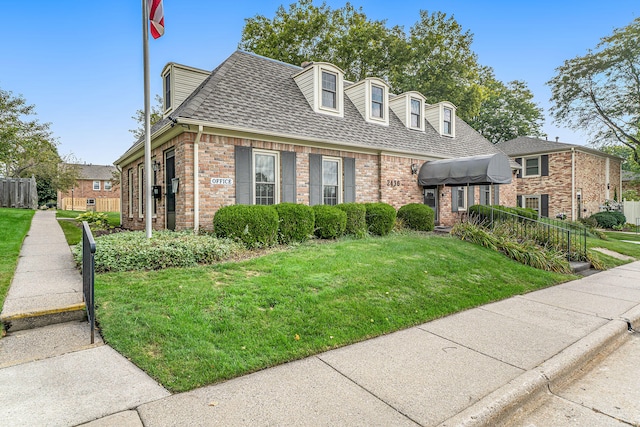 view of front of home featuring a shingled roof, brick siding, fence, and a front lawn