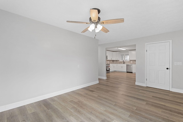 unfurnished living room with light wood-style floors, a ceiling fan, baseboards, and a sink