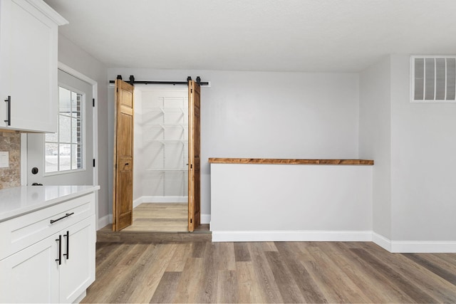 unfurnished dining area with visible vents, light wood-style flooring, baseboards, and a barn door