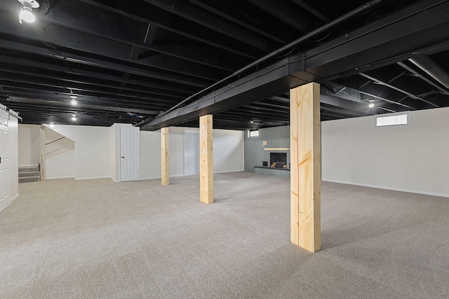 below grade area with a fireplace with raised hearth, stairway, carpet flooring, and baseboards