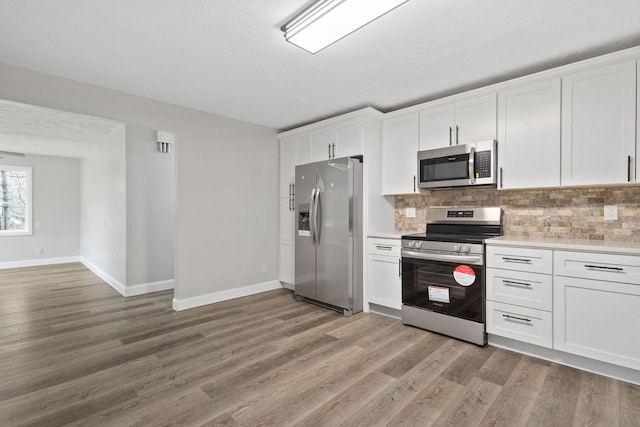 kitchen with white cabinets, stainless steel appliances, light countertops, light wood-style floors, and backsplash