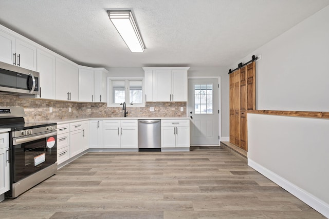 kitchen featuring a healthy amount of sunlight, white cabinetry, a barn door, and appliances with stainless steel finishes