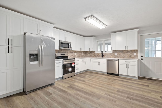 kitchen with tasteful backsplash, light countertops, light wood-style flooring, appliances with stainless steel finishes, and white cabinetry