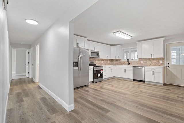 kitchen featuring white cabinets, decorative backsplash, appliances with stainless steel finishes, light countertops, and light wood-type flooring