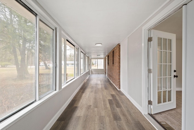 hallway featuring brick wall, visible vents, baseboards, and wood finished floors