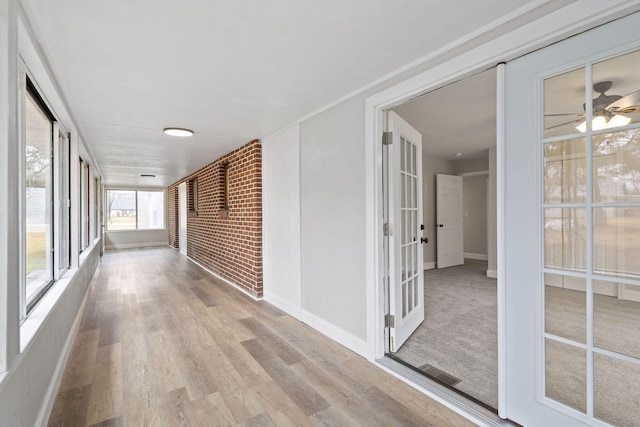 hall featuring baseboards, visible vents, brick wall, and wood finished floors