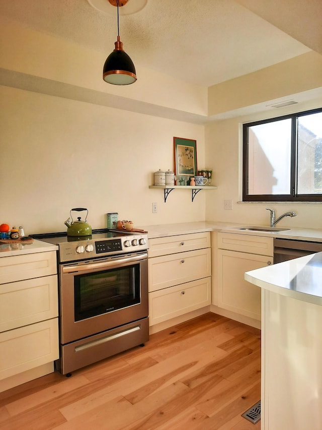 kitchen with light wood-style flooring, a sink, light countertops, stainless steel electric range oven, and pendant lighting