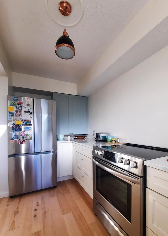 kitchen featuring stainless steel appliances, light countertops, hanging light fixtures, white cabinets, and light wood-type flooring