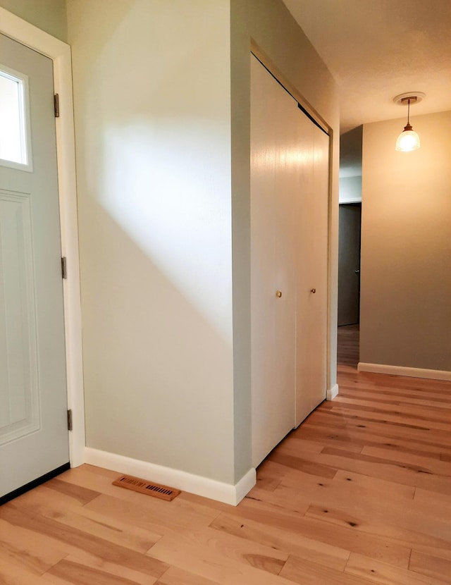 hall featuring baseboards, visible vents, and light wood-style floors