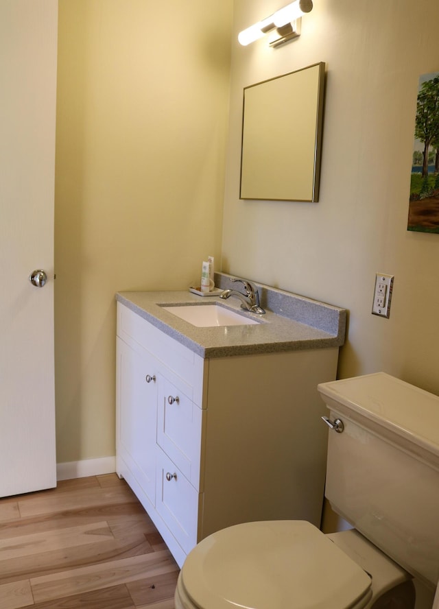 half bath featuring wood finished floors, vanity, toilet, and baseboards