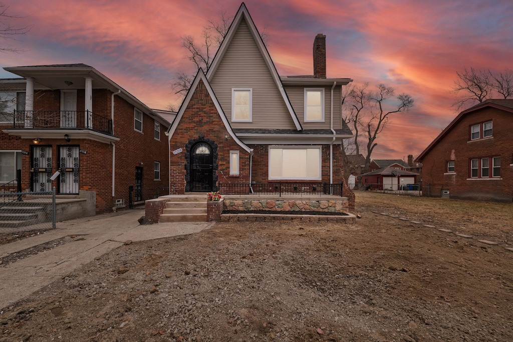 view of front of home with brick siding, fence, a chimney, and a balcony