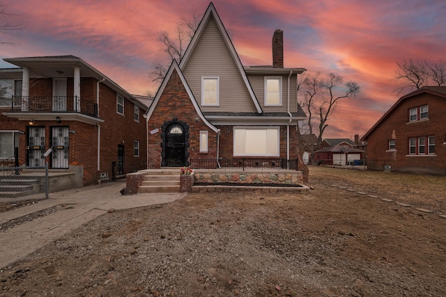 view of front of home with brick siding, fence, a chimney, and a balcony