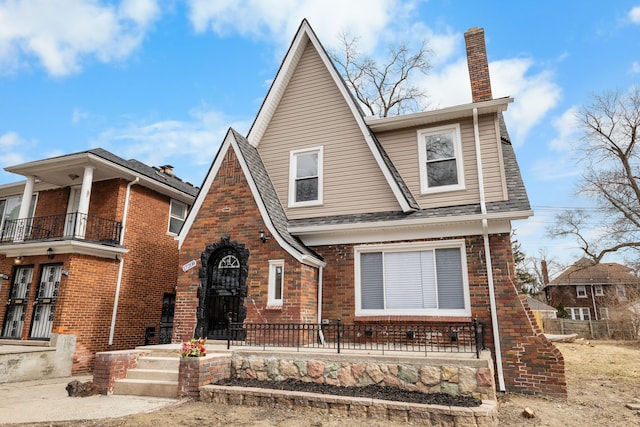 view of front facade featuring a balcony, roof with shingles, a chimney, and brick siding