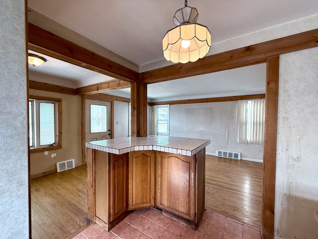 kitchen with light wood-type flooring, visible vents, tile counters, and beam ceiling