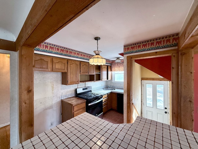 kitchen with tile countertops, stainless steel gas range, a sink, and pendant lighting