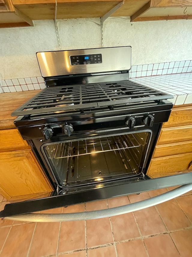 interior details with stainless steel gas range, backsplash, and tile countertops