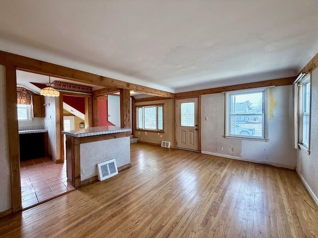 kitchen featuring light wood-type flooring, baseboards, visible vents, and beamed ceiling