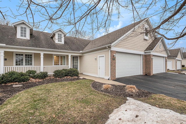 new england style home featuring roof with shingles, brick siding, a porch, a garage, and a front lawn