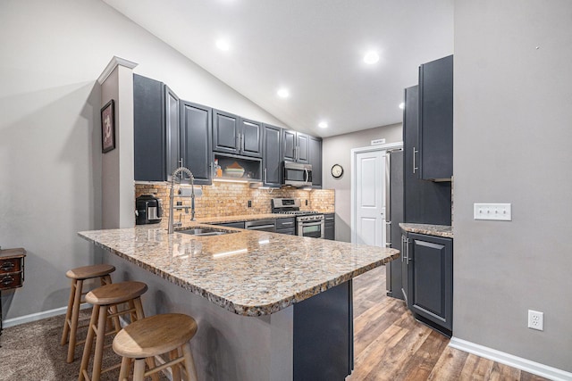 kitchen featuring lofted ceiling, appliances with stainless steel finishes, a sink, a peninsula, and a kitchen bar