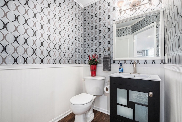 half bath featuring toilet, a wainscoted wall, wood finished floors, vanity, and wallpapered walls