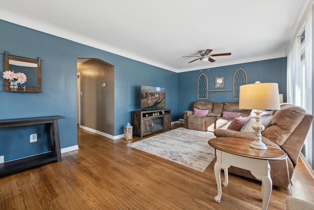 living room with baseboards, arched walkways, wood finished floors, and a ceiling fan