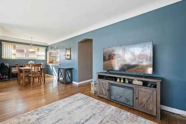 living area with baseboards, arched walkways, and wood finished floors