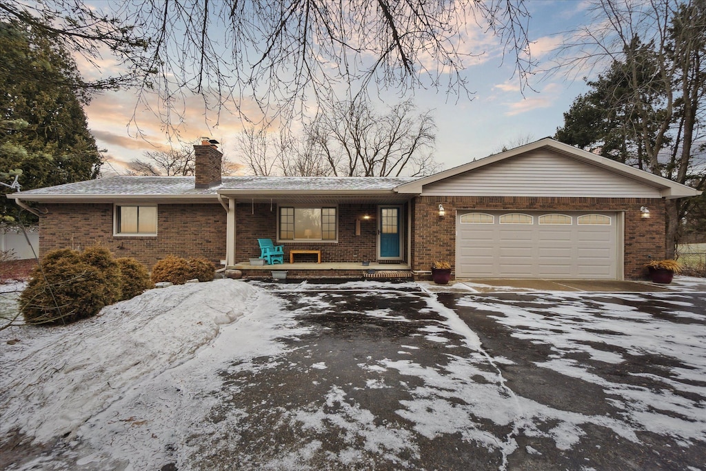 single story home with a garage, driveway, a chimney, covered porch, and brick siding