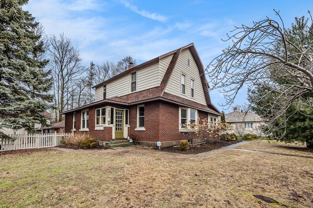 view of side of home featuring entry steps, a gambrel roof, fence, a yard, and brick siding