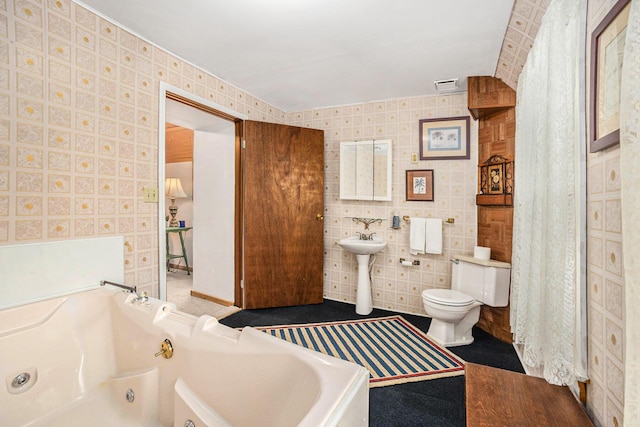 full bathroom featuring toilet, a tub with jets, and wallpapered walls