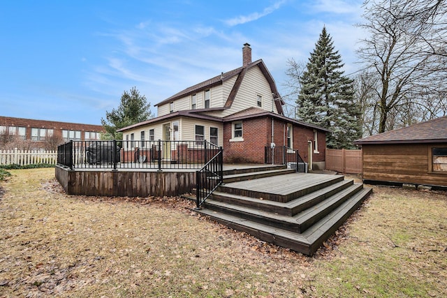 rear view of property featuring a gambrel roof, a chimney, fence, a deck, and brick siding