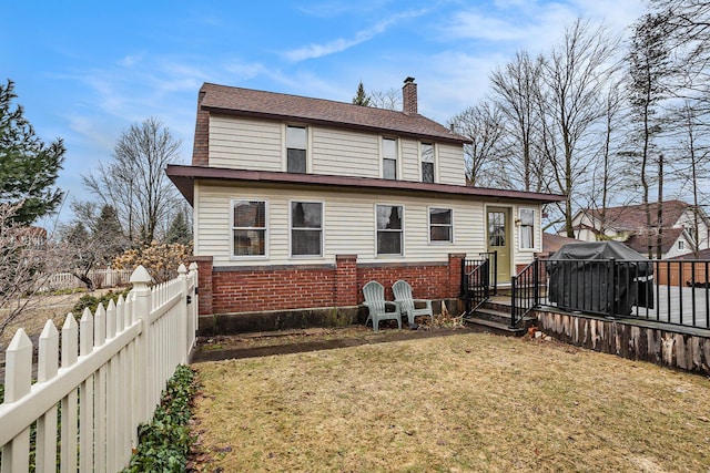 back of property featuring a wooden deck, a fenced backyard, a chimney, a yard, and brick siding