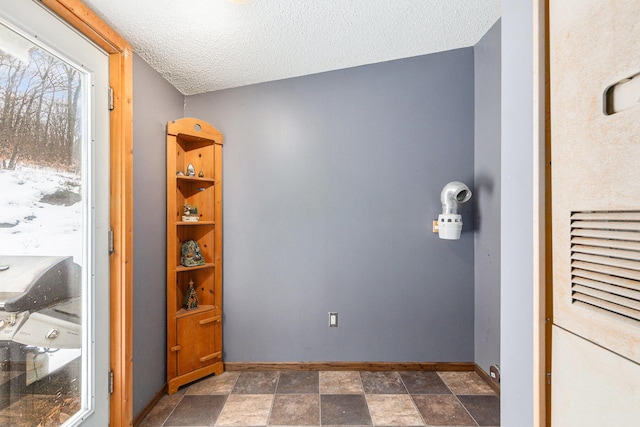 interior space with a textured ceiling, stone finish flooring, and baseboards