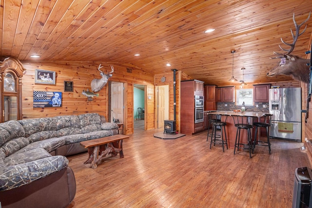 living area featuring a wood stove, wooden ceiling, light wood-style flooring, and vaulted ceiling