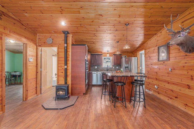 kitchen with a breakfast bar, wood ceiling, light wood-style floors, stainless steel fridge, and a wood stove