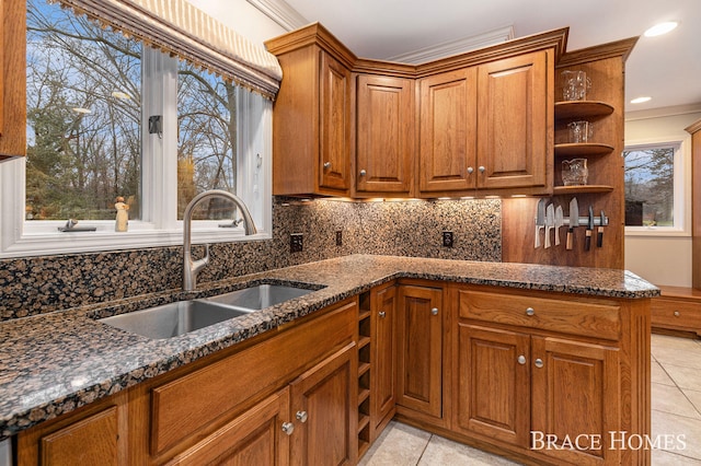 kitchen featuring brown cabinetry, dark stone counters, a sink, and open shelves