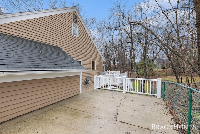 view of side of home with a shingled roof, a patio area, and fence