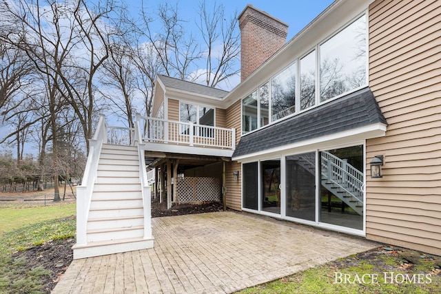 rear view of property featuring a patio, a chimney, stairway, roof with shingles, and a deck