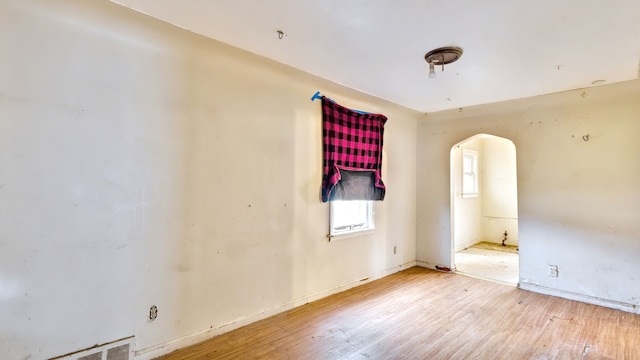 empty room featuring arched walkways, visible vents, baseboards, and wood finished floors