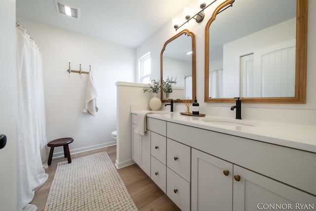 full bath with toilet, a sink, visible vents, baseboards, and double vanity