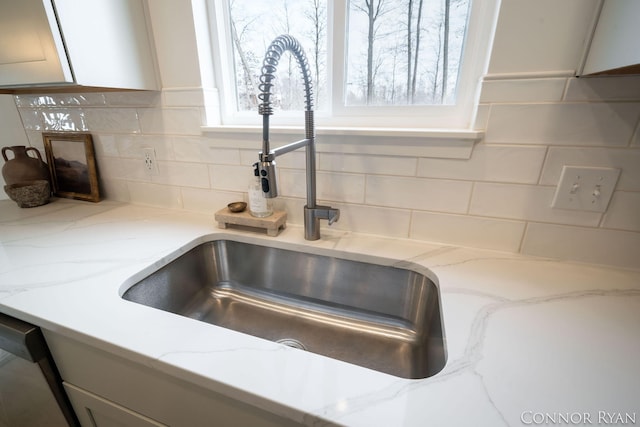 room details with dishwasher, tasteful backsplash, light stone counters, and a sink