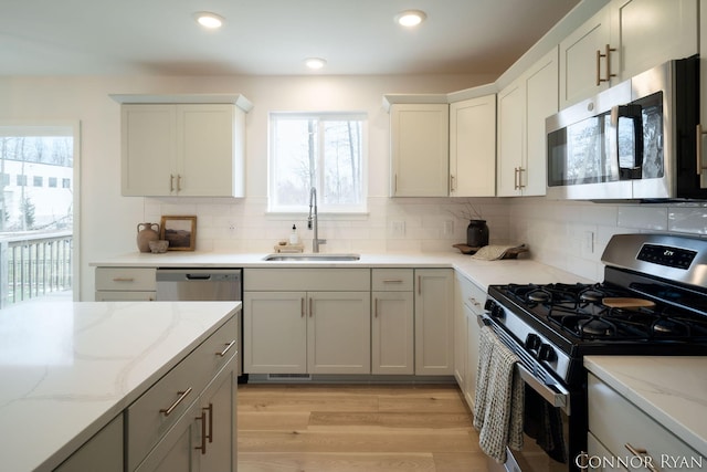 kitchen featuring recessed lighting, stainless steel appliances, a sink, light wood-type flooring, and light stone countertops