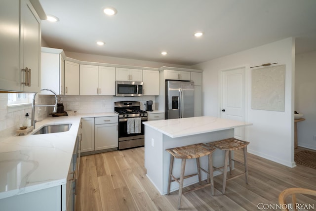 kitchen with light wood-style flooring, stainless steel appliances, a sink, backsplash, and a center island