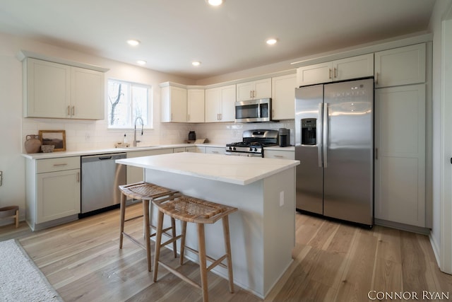 kitchen featuring light wood finished floors, tasteful backsplash, appliances with stainless steel finishes, a sink, and a kitchen island