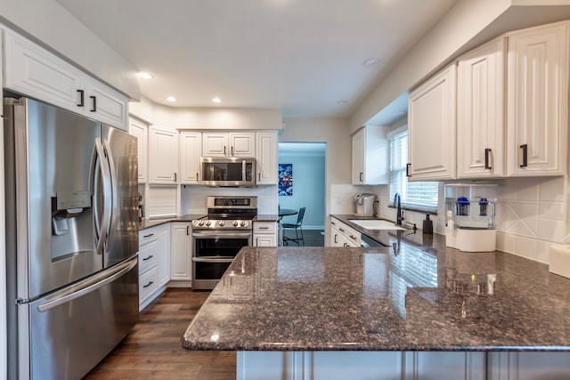 kitchen featuring dark wood-style flooring, a peninsula, stainless steel appliances, white cabinetry, and a sink